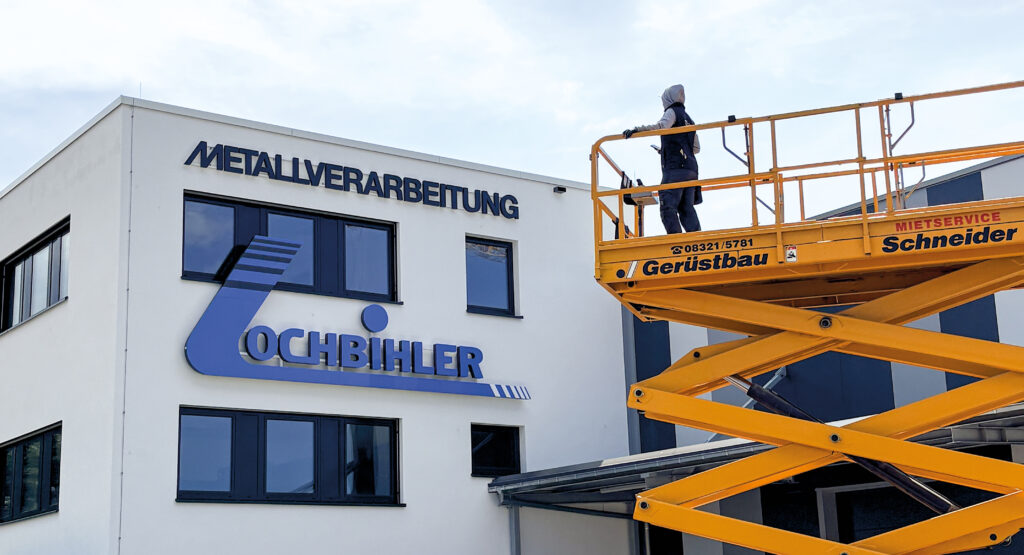Mitarbeiter von mica Das Werbewerk montiert Fassadenwerbung an einem Firmengebäude in Sonthofen